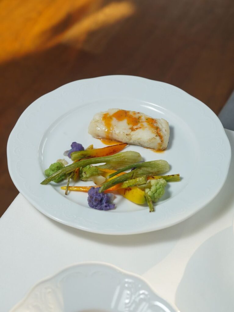 A refined seafood dish with vegetables served on an elegant white plate under natural light.