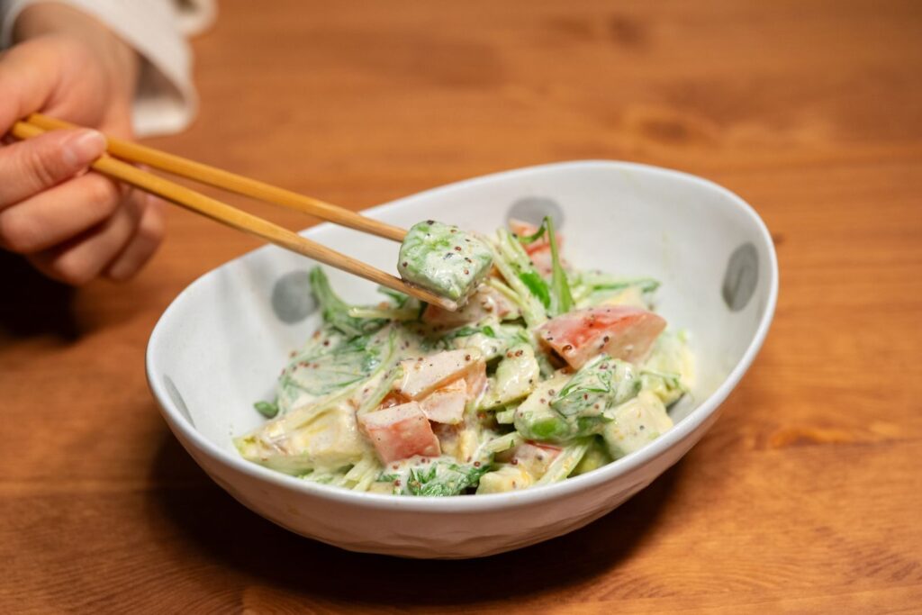 Vibrant Asian salad with veggies, mixed in creamy dressing, served with chopsticks.