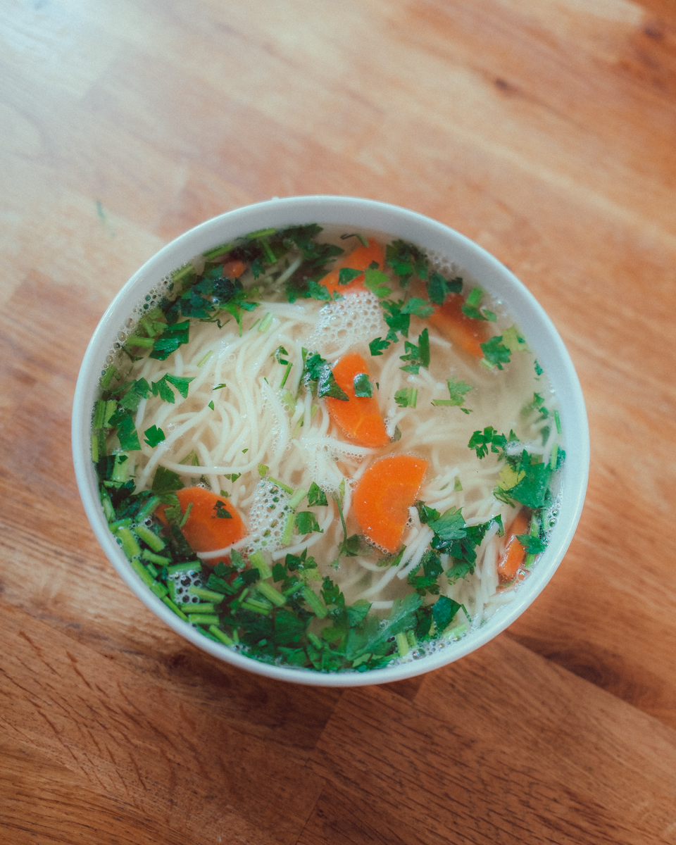 A bowl of traditional Polish chicken noodle soup with carrots and parsley on a wooden table.
