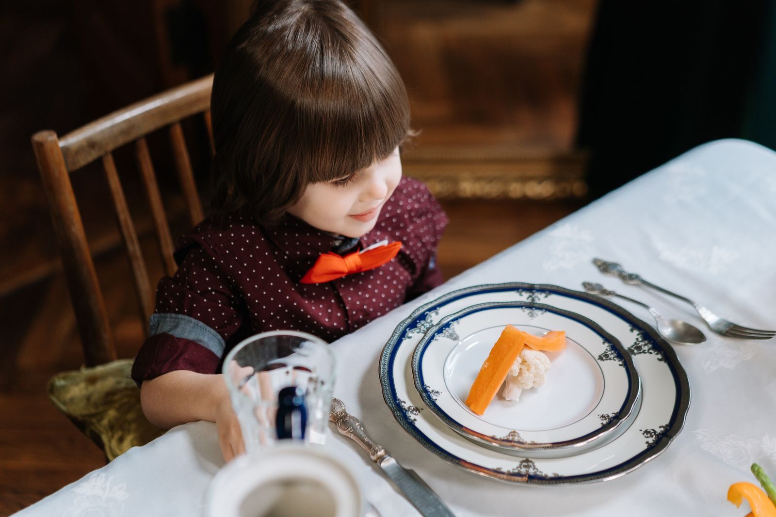 A young child wearing a bow tie seated at a beautifully set dining table.