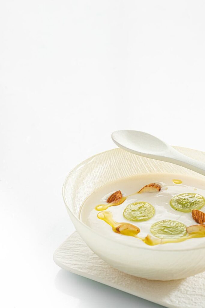 Minimalist dessert dish with grapes, almonds, and cream on a white background, capturing a refined culinary presentation.