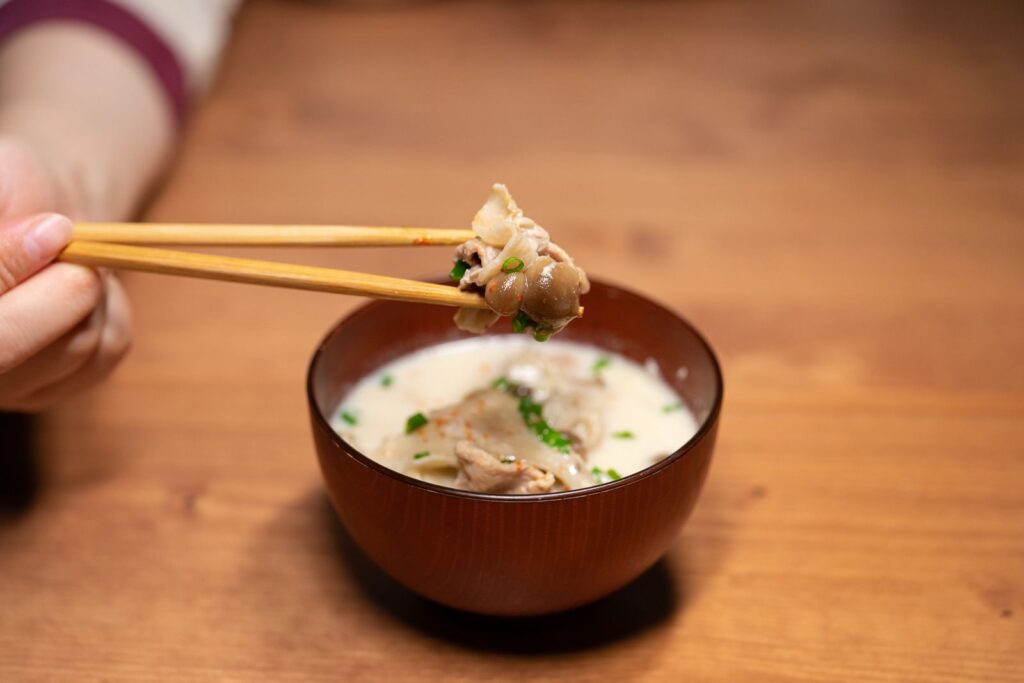Delicious Asian soup in a wooden bowl held with chopsticks, perfect for a culinary experience.