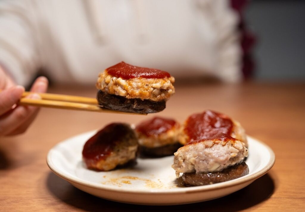 Close-up of a gourmet mushroom topped with meat and tomato sauce, held with chopsticks.