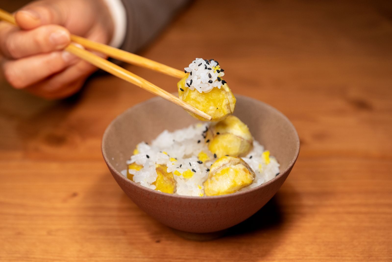 Close-up of a bowl of rice with vegetables being picked up by chopsticks indoors.