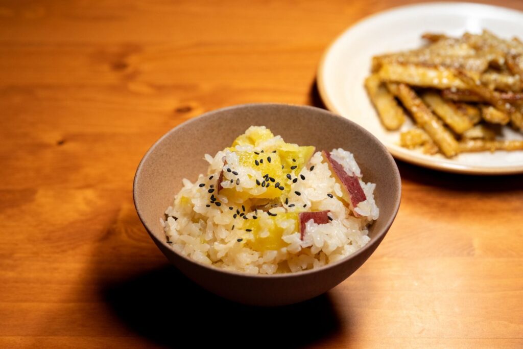Delicious bowl of Japanese sweet potato rice topped with sesame seeds, served on a wooden table.