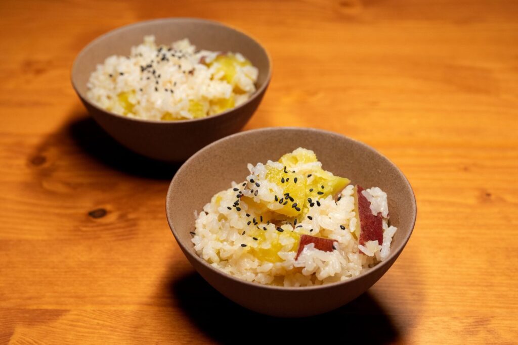 Two bowls of Asian rice with sweet potatoes and black sesame seeds on a wooden table.