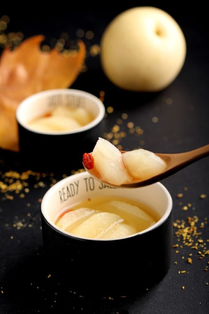 Beautifully presented dessert bowl featuring sliced pears and goji berries, styled with an autumnal theme.
