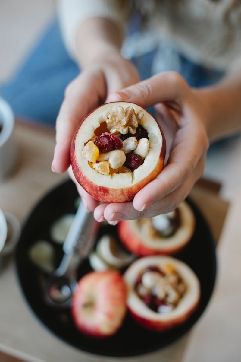 From above of crop anonymous female cook demonstrating tasty fresh apple stuffed with nuts and assorted dried fruits in house