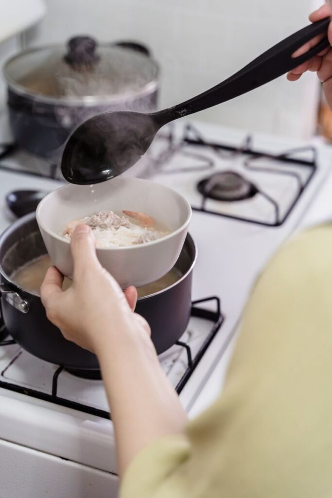 A woman cooking soup on a stove with steam rising, capturing a warm home-cooking feel.