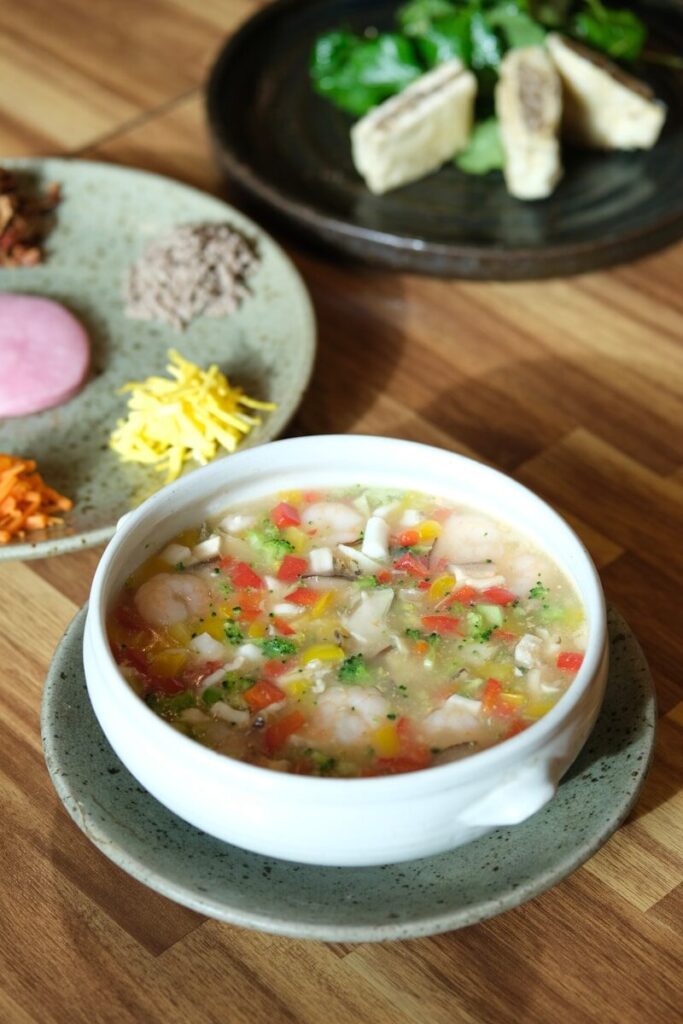 a bowl of soup sits on a table next to a plate of food