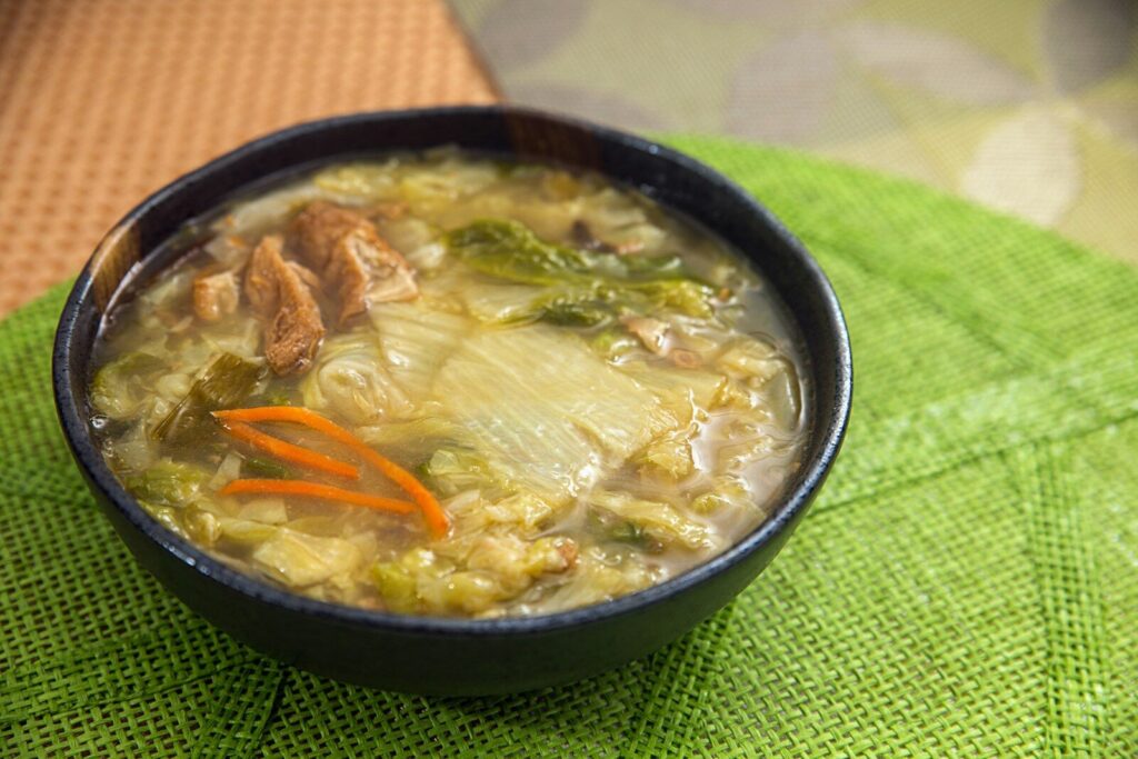 A bowl of vegetable soup with cabbage and carrots on a green placemat